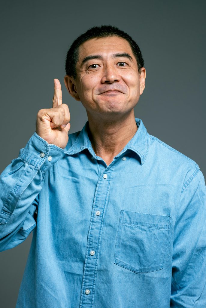 pexels-photo-4584186-4584186 Smiling man in casual blue shirt pointing upward, suggesting an idea or realization.